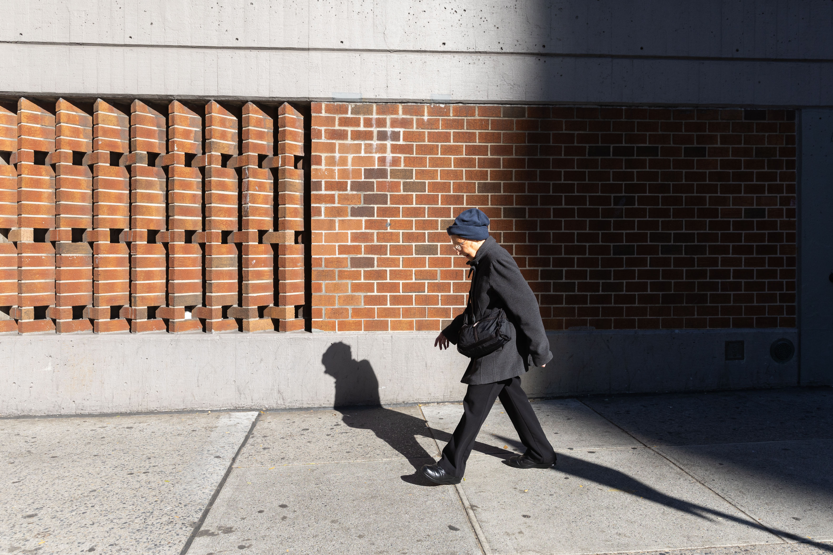 A photo of a senior woman wearing winter clothes walking on the sidewalk in the Upper West Side of New York City.