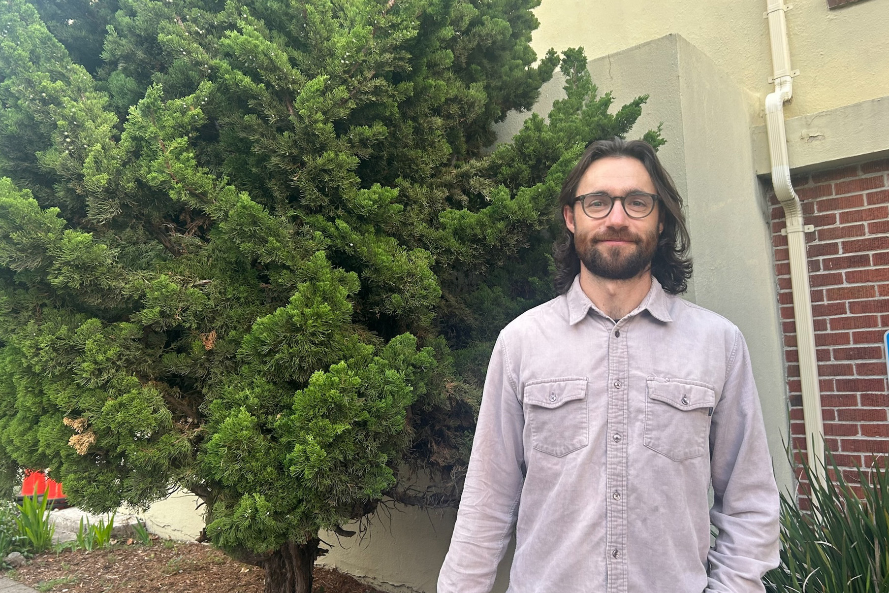A portrait of a man smiling beside a tree.